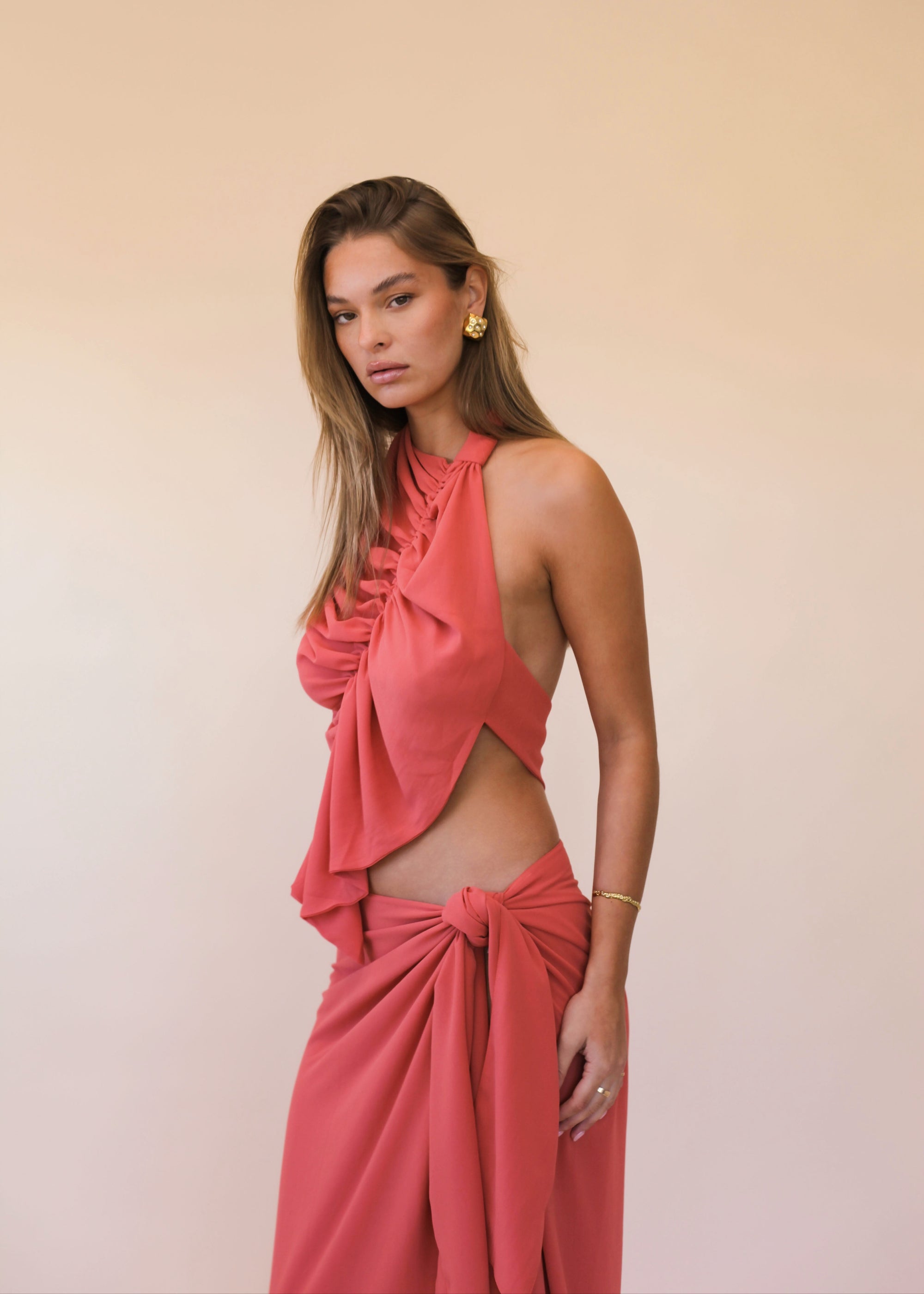 Woman wearing a coral orange halter top and skirt set against a beige background