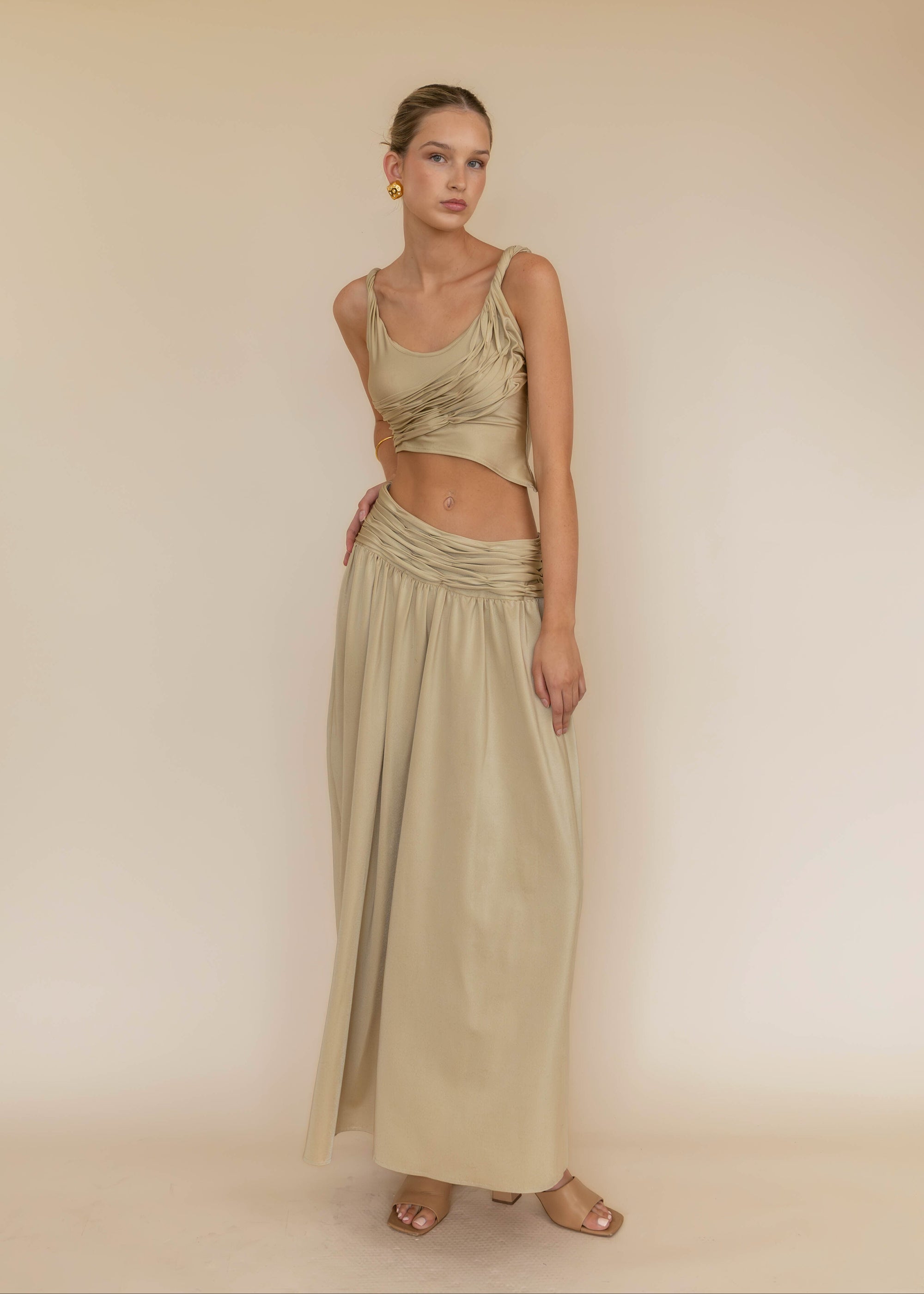 Woman wearing a green top and long skirt against a beige background