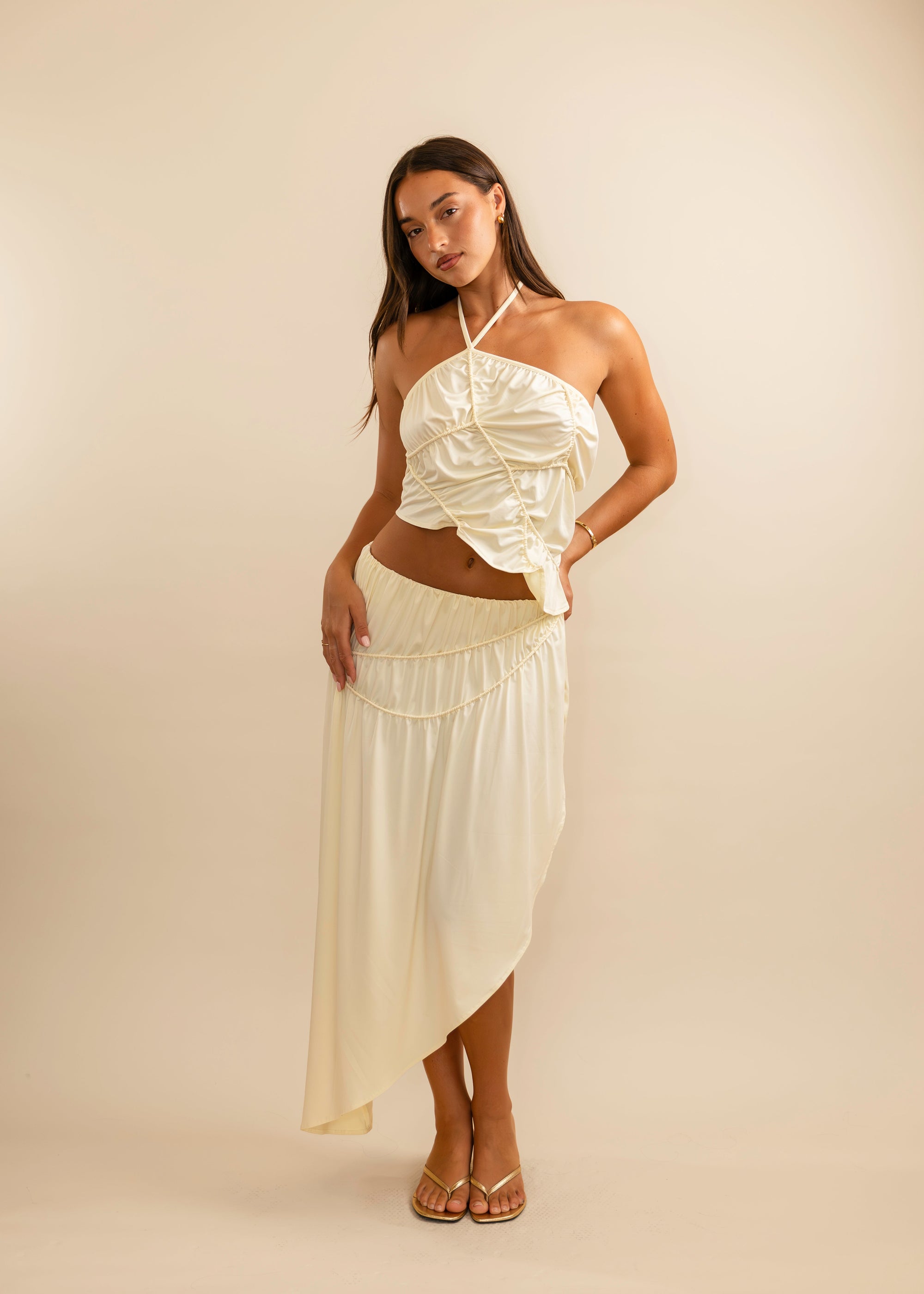 Woman wearing a cream halter top and skirt against a beige background