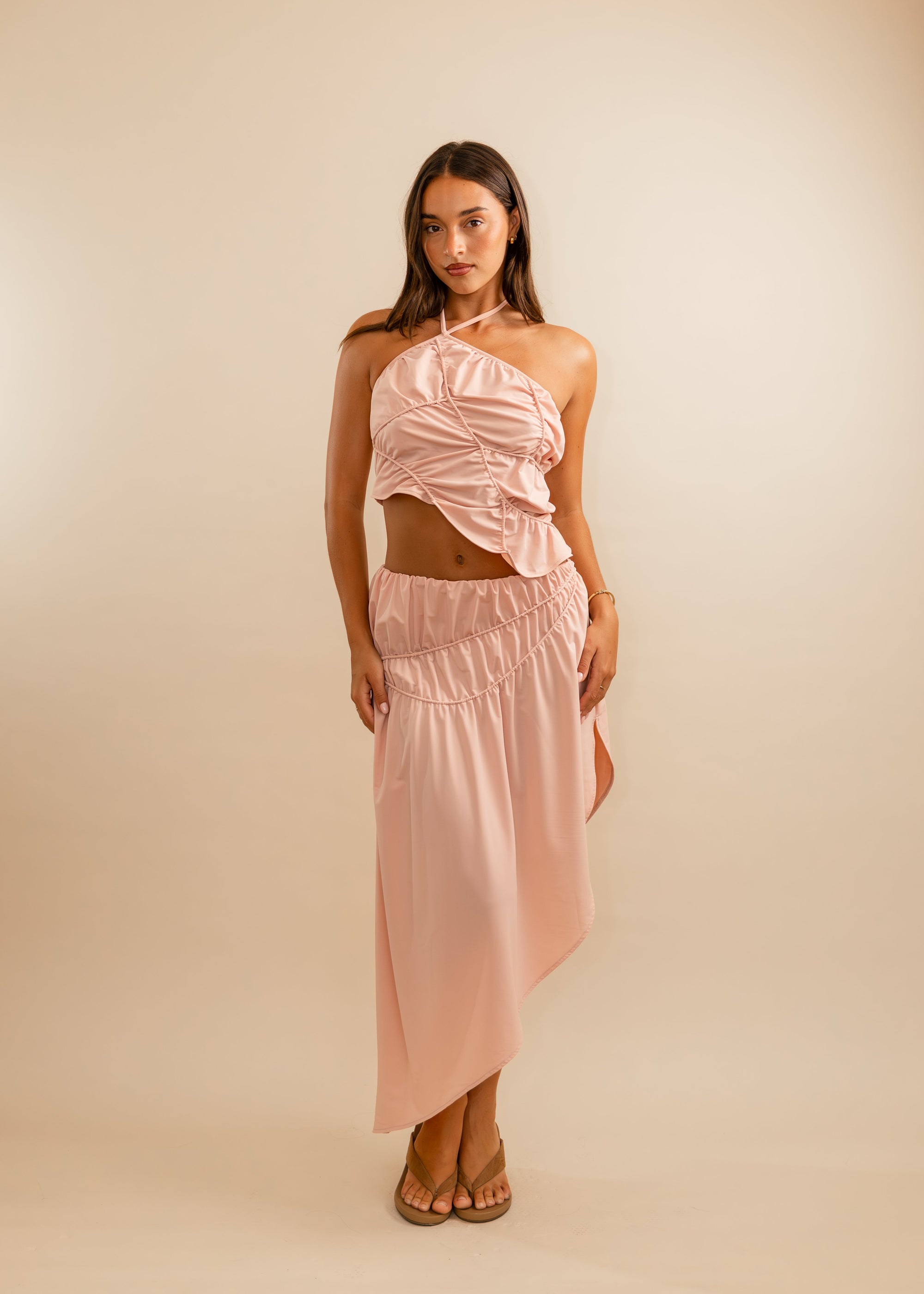 Woman wearing a pink blush halter top and skirt against a beige background