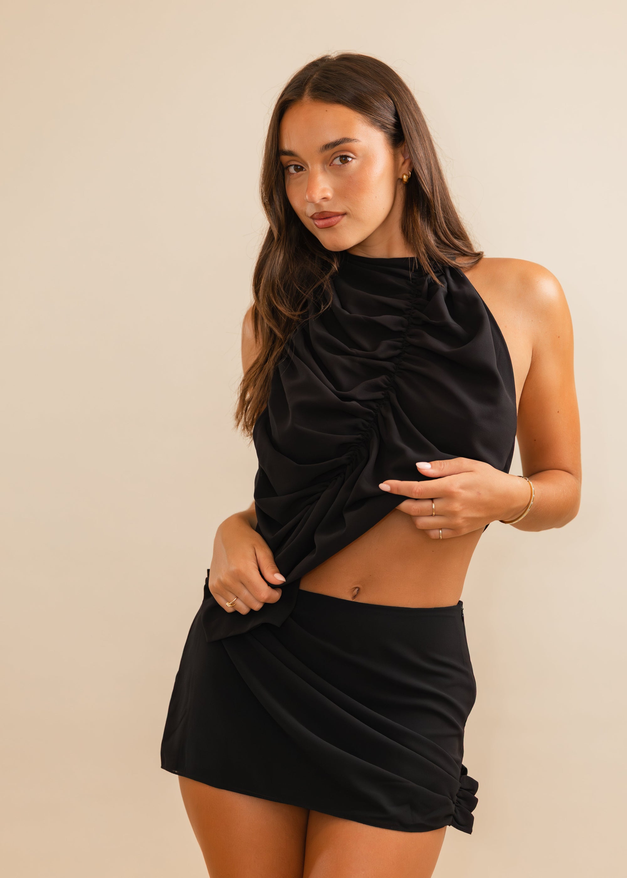 women standing in a black mini skirt set with draping and ruching in front of a plain background 