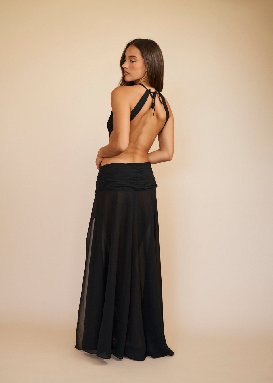 Woman wearing a black halter top and long skirt against a beige background