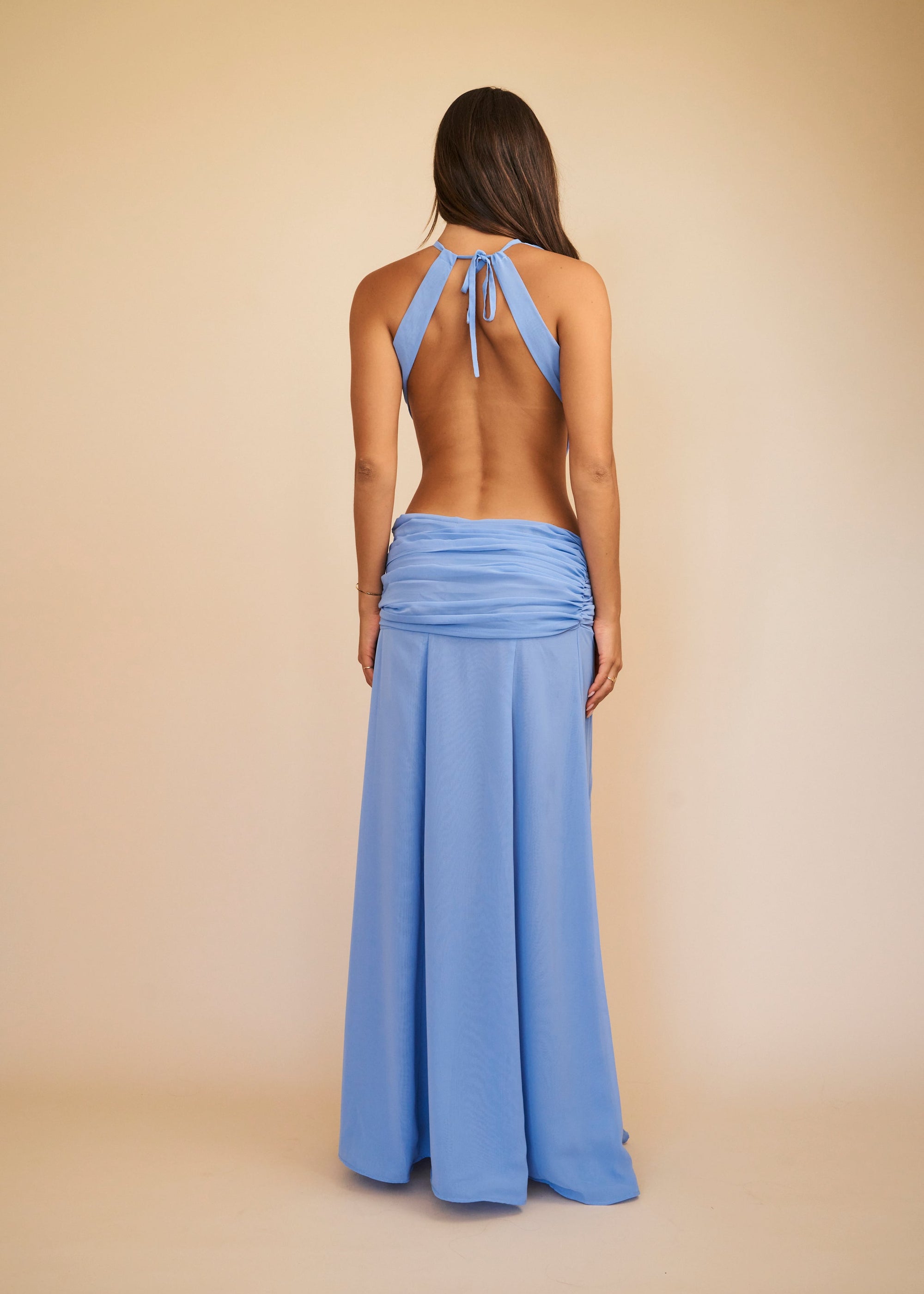 Woman wearing a blue halter top and wide-leg pants on a beige background