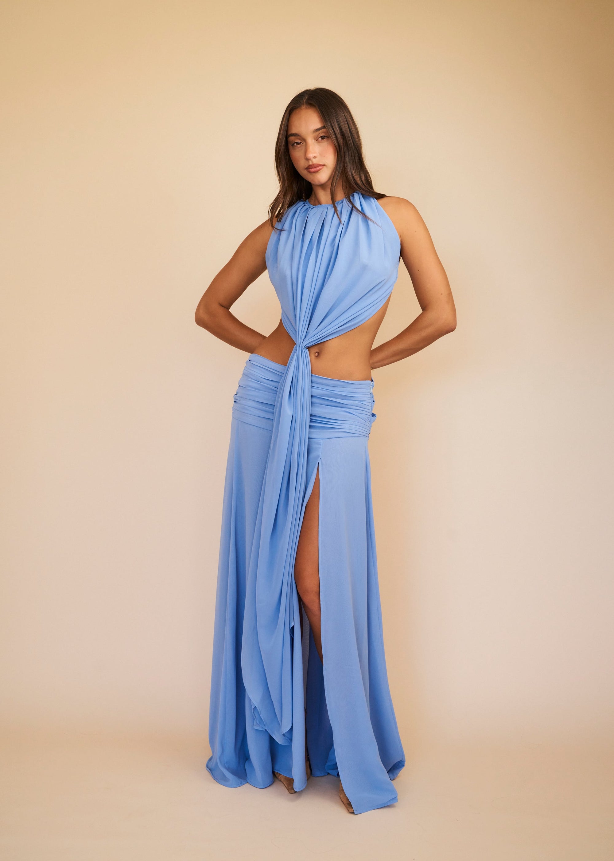 Woman wearing a blue halter neck dress with a slit on a beige background