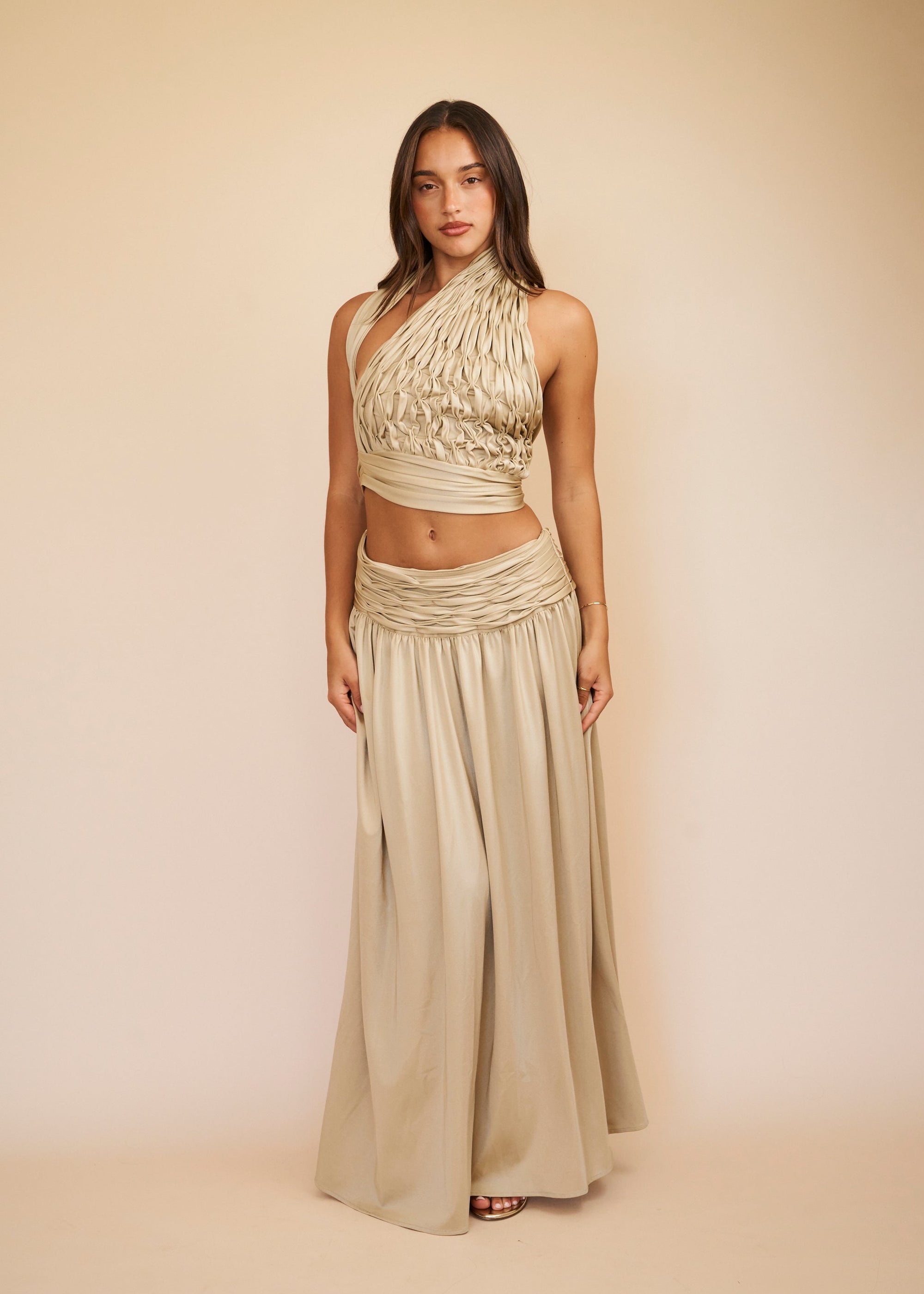 Woman wearing a beige halter top and long skirt against a beige background