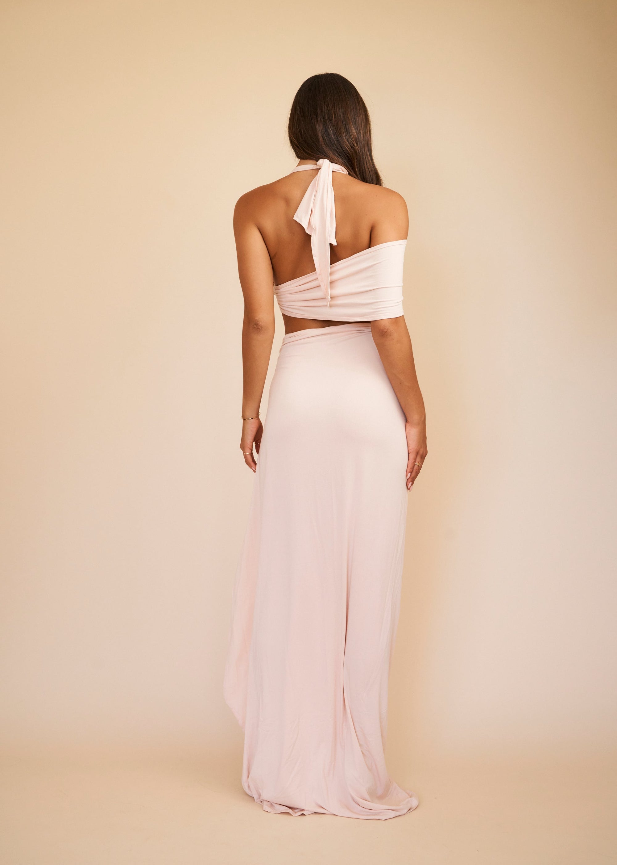 Woman wearing a light pink gown with a sheer overlay on a beige background