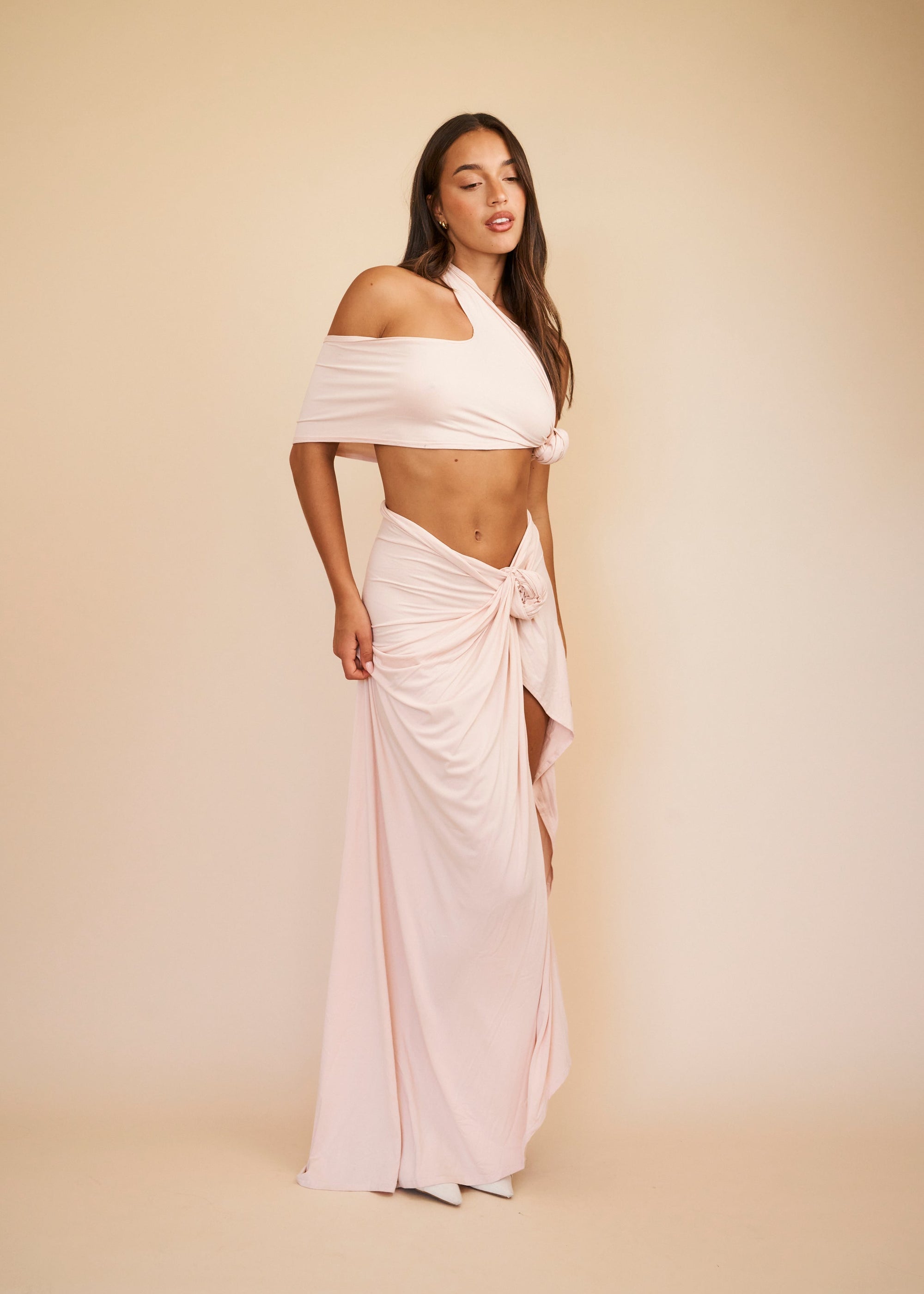 Woman wearing a white off-shoulder top and flowing skirt against a beige background