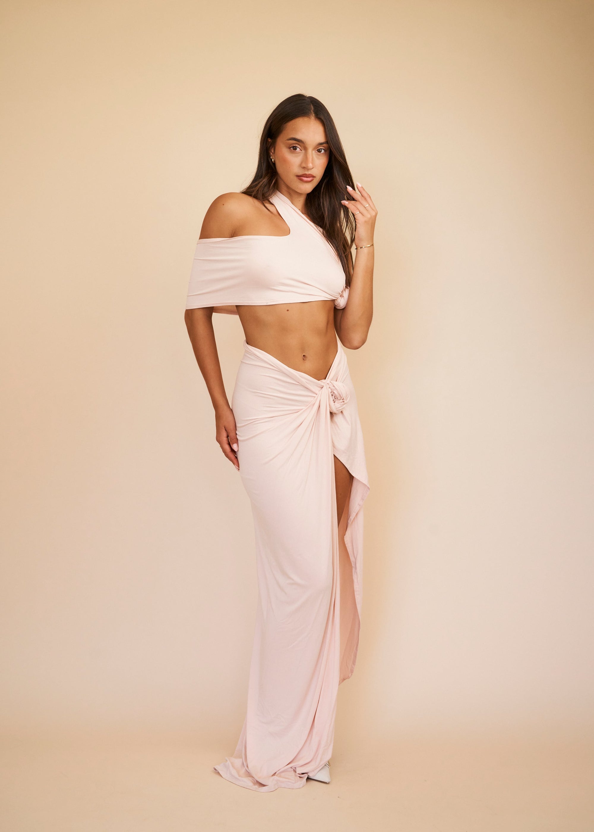 women wearing a blush pink crop top and maxi skirt set standing in front of a beige background 