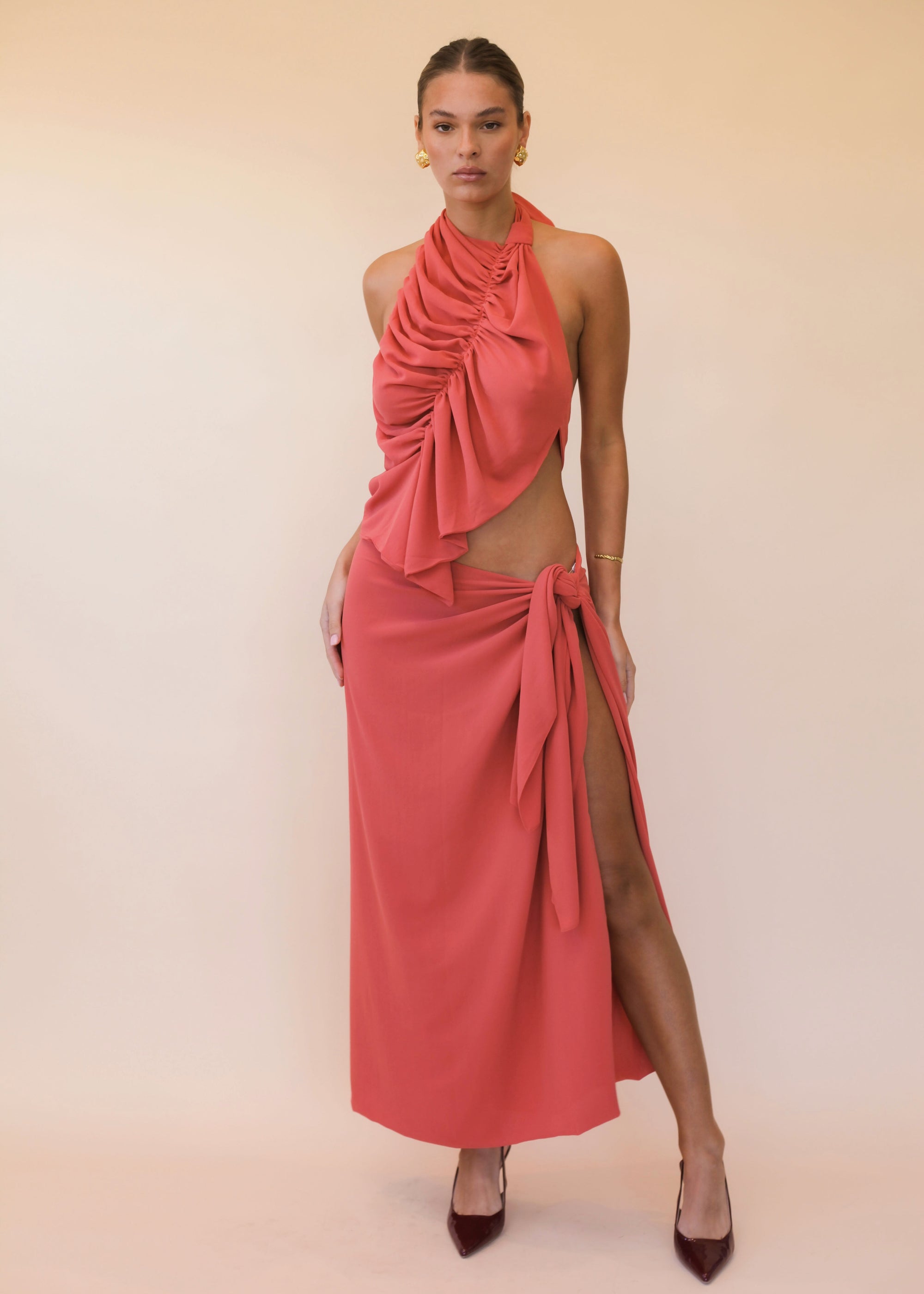 Woman wearing a coral halter neck set with a slit on a beige background
