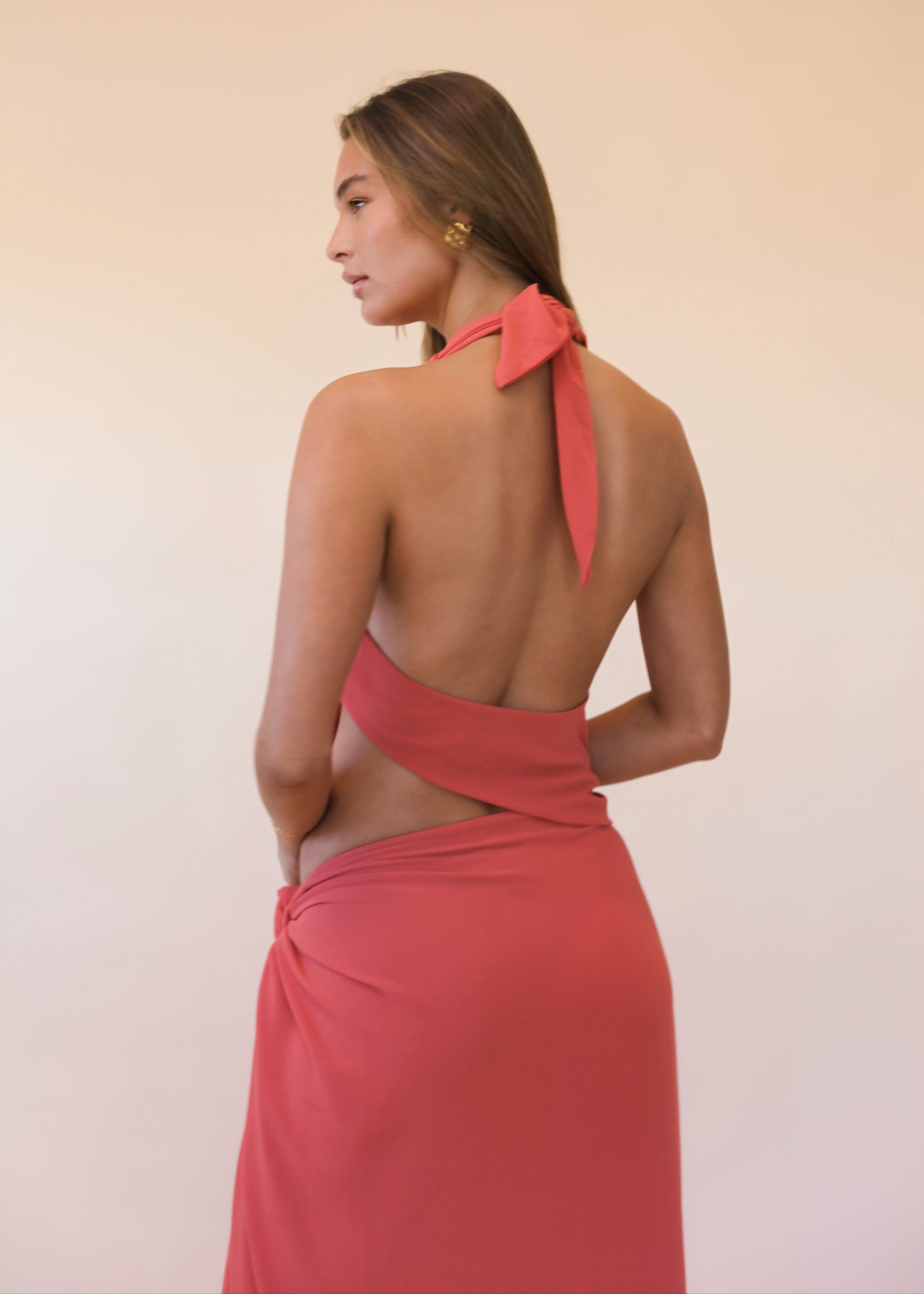 Woman wearing a orange halter neck dress with open back detail on a beige background