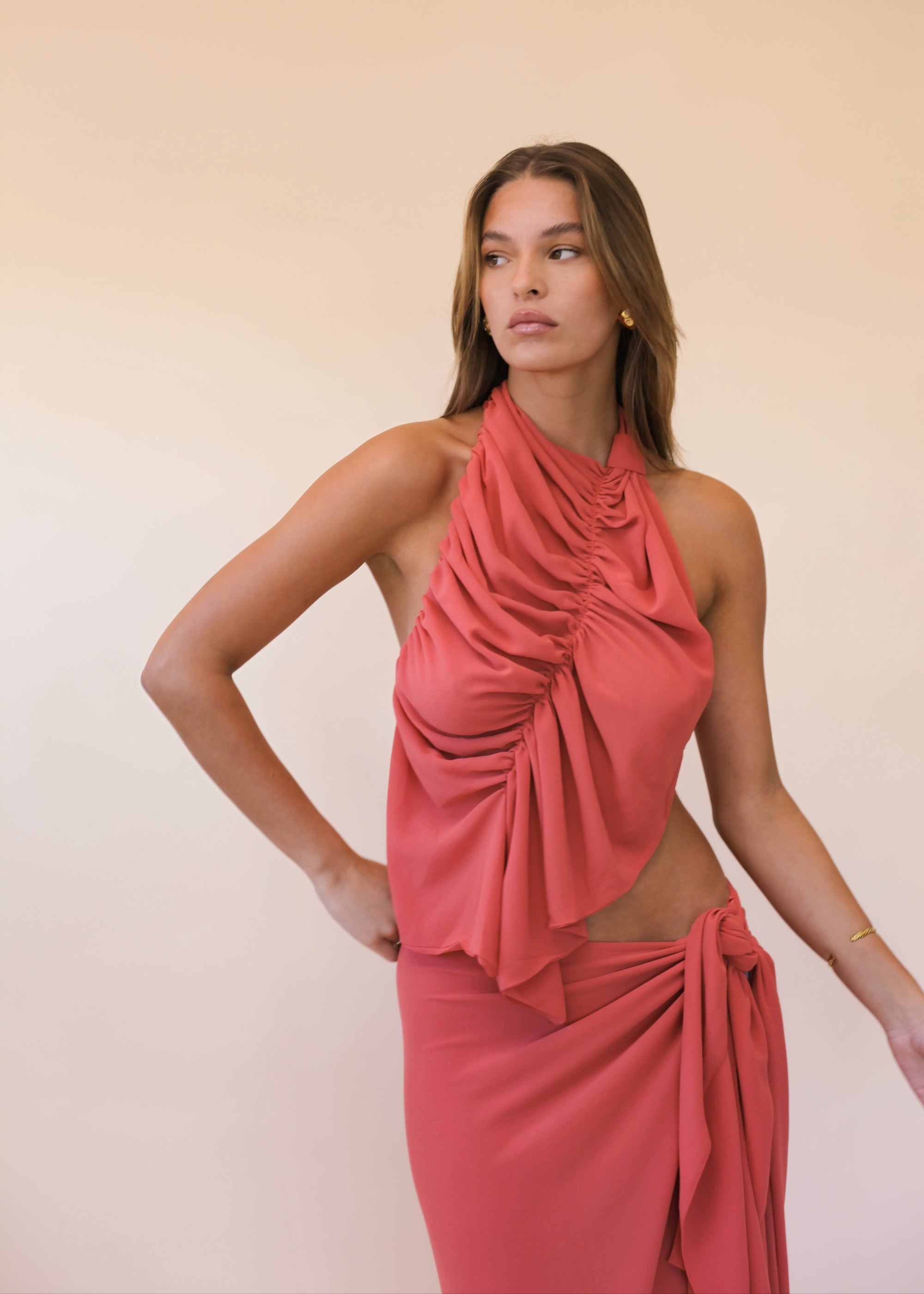 Woman wearing a coral halter neck dress against a plain background