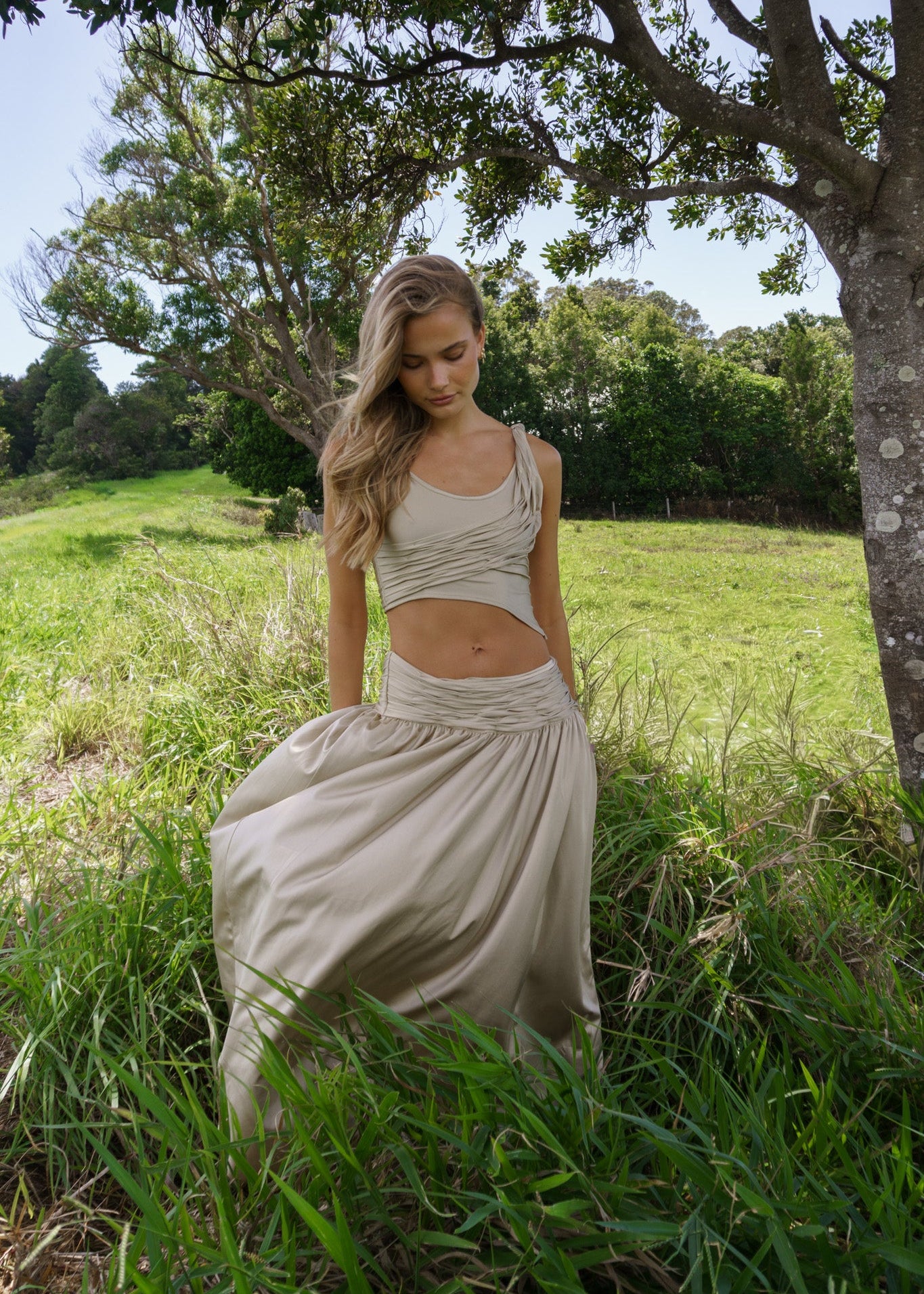 Woman in a flowing dress standing in a grassy field with trees in the background
