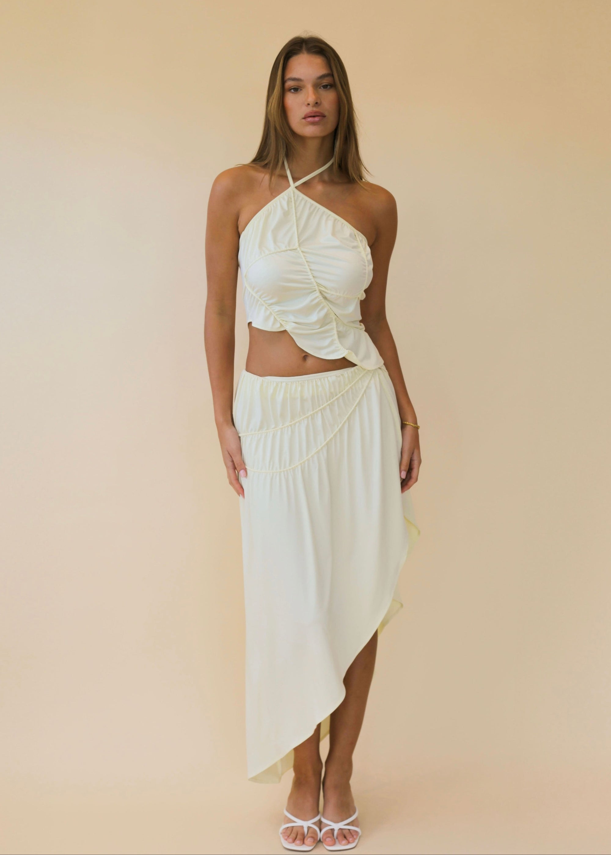 Woman wearing a white halter top and skirt against a beige background