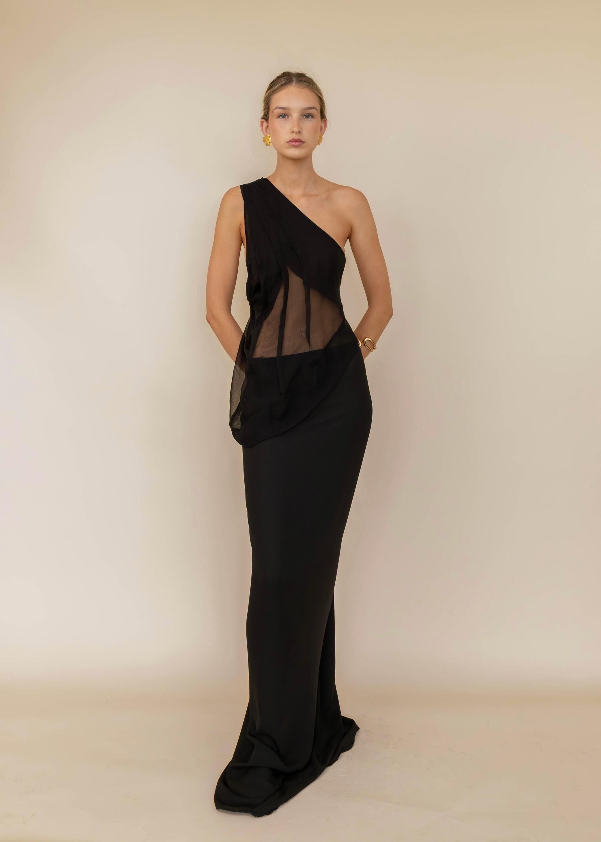 Woman wearing a black one-shoulder dress against a beige background