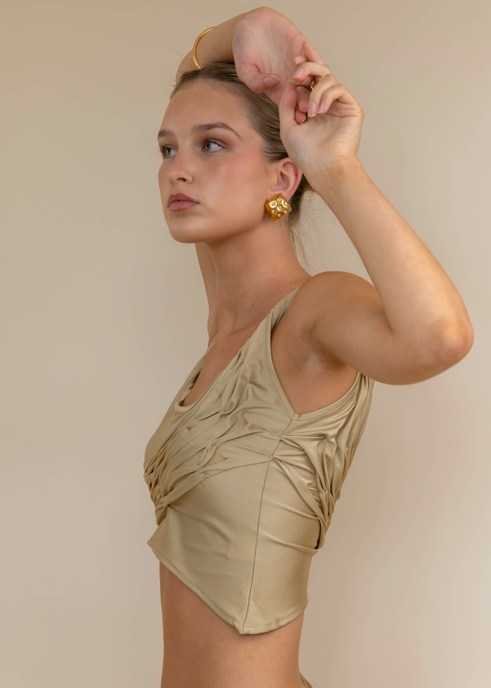 Woman wearing a beige sleeveless top against a plain background