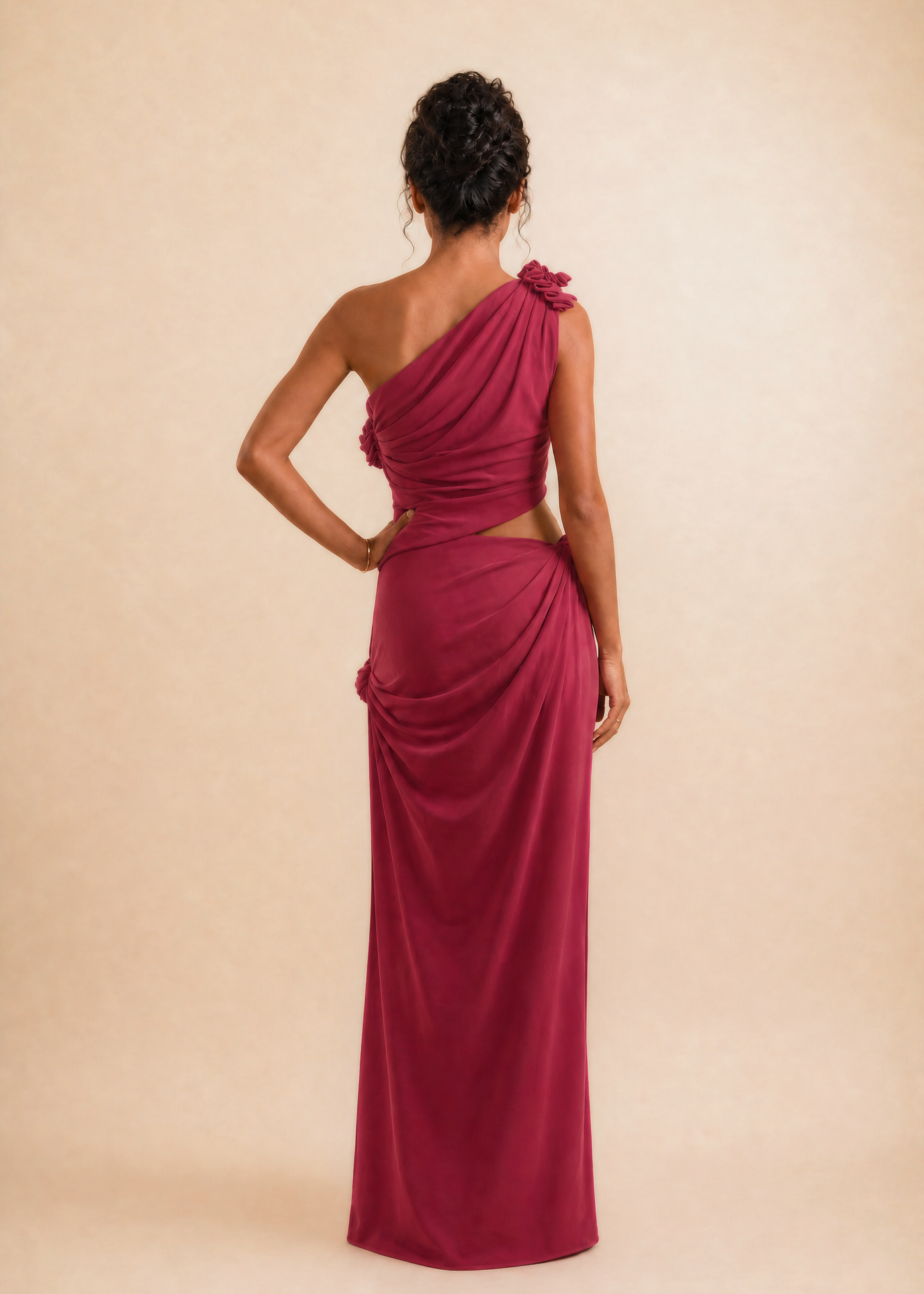 A woman modeling a floor-length, one-shoulder magenta dress from the back, standing against a solid beige studio backdrop.