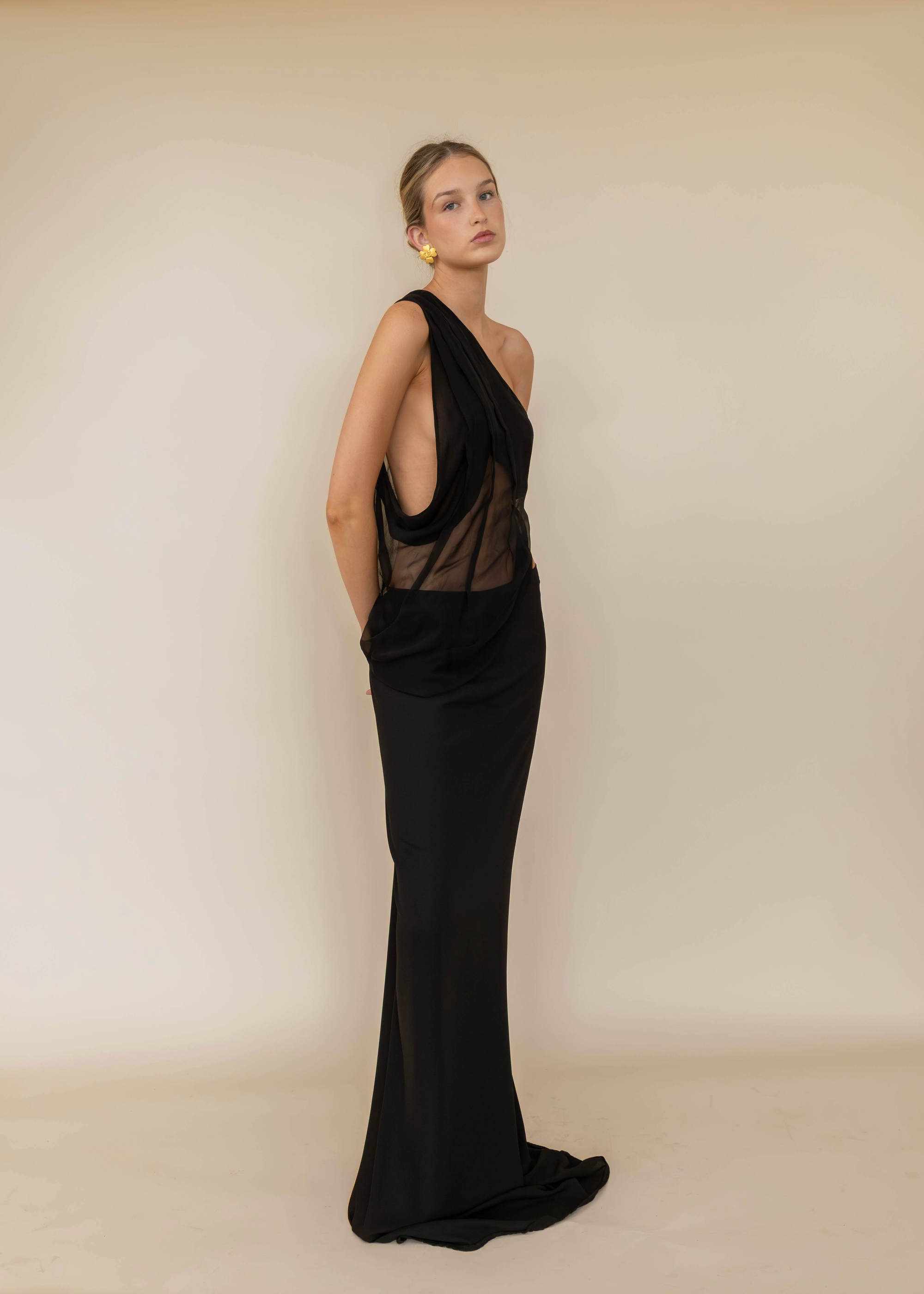 Woman wearing a black one-shoulder gown against a beige background
