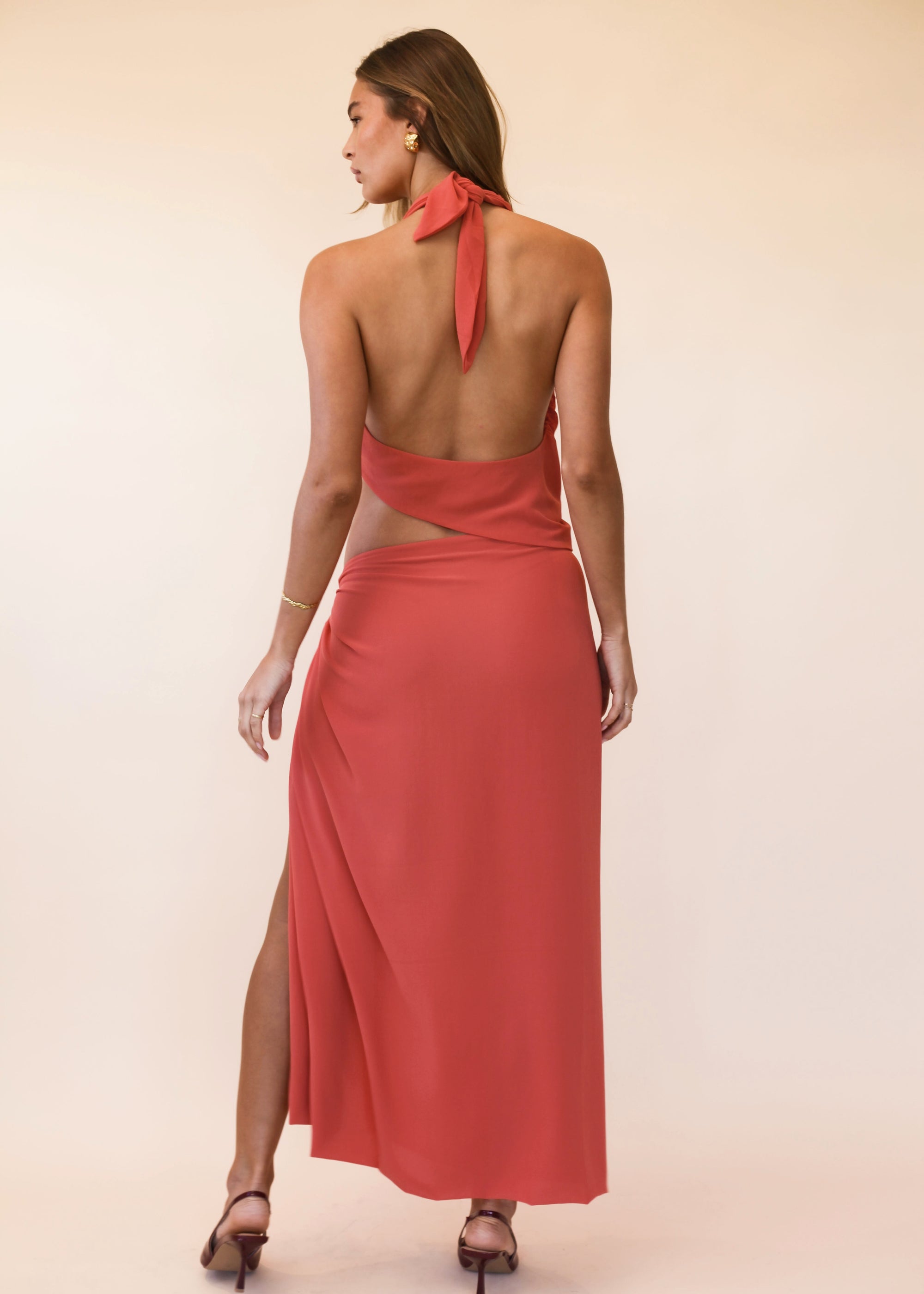 Woman wearing a coral orange halter neck dress with a slit on a beige background