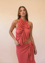 Woman wearing a coral halter neck dress against a plain background